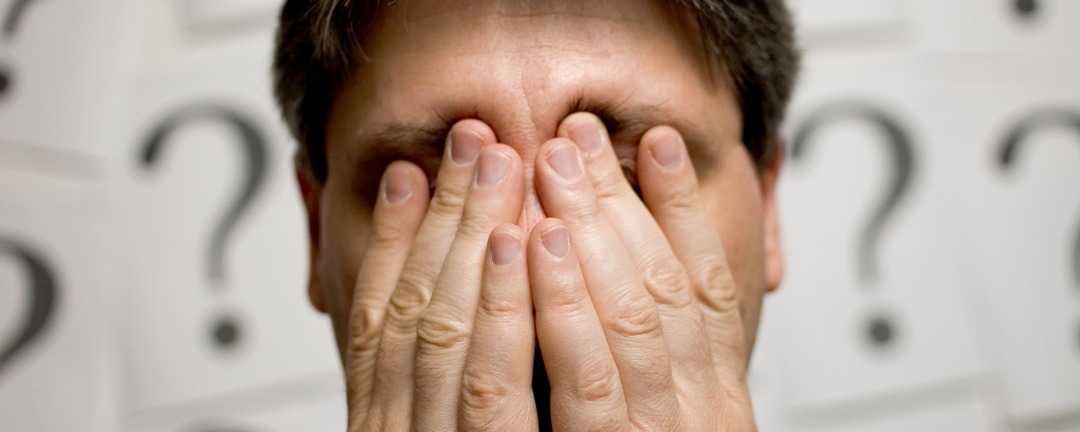 man with hands over face stressed with question marks as background